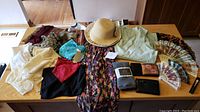 Full lot view showing all clothing and accessories spread on a table including scarves, sunhats, robe, sundress, wallet, and fans.