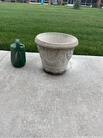 Photo showing one concrete planter and one green plastic watering can on concrete patio with grass in background