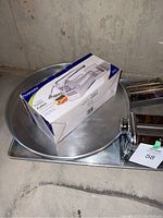 Photo showing the boxed ProGarden potato cutter on top of round metal baking pan and rectangular baking tray, pasta maker partially visible.