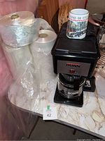 Bunn coffee maker with glass pot, ceramic mug, and rolls of produce bags on countertop.