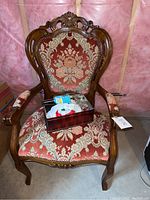 Front view of the carved wooden armchair upholstered in floral fabric with sewing kit box placed on the seat