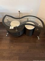 Full view of the glass top coffee table showing the curvy glass surface, metal legs, dark wood base, and the white stools tucked underneath.