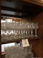 Shelf displaying 17 matching crystal wine glasses and 1 larger wine glass in a wooden cabinet.