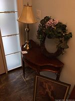 Photo showing wood entryway table, brass-colored lamp, and grapevine wreath on top with artificial flowers.