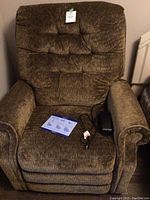 Front view of the brown fabric power recliner chair with remote control and manual on seat.