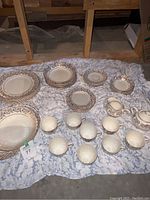 Full set arranged on blanket showing various plates, bowls, cups, and serving pieces with gold floral trim detail