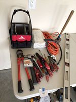 View of the full set showing the Husky tool bag with dividers, bolt cutters, pliers, screwdrivers, snips, work gloves, sledgehammer, extension cord, level, and measuring tape on a white table.