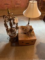 Photo showing two metal table lamps and a cardboard box with light fixture parts on a basement floor with pink insulation visible.
