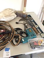 Photo of lot including Makita drill, jumper cables, gloves, axe, hammer, spirit level, and small hardware set.