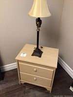 Front view of nightstand with two drawers and decorative lamp on top, showing wood grain and knob details.