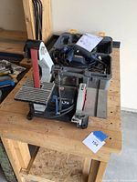 Both sanders on wooden workbench. Ryobi sander inside open plastic case with instruction manual. Delta sander with belt and disc sanding surfaces on metal base.