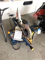 Front-right angle of saw on floor with handle, sliding rails, manual under fence.