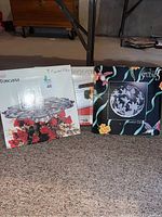 Boxes of Toscana crystal platter, Paradise Garden decorative plate, and Tramontina silver dish placed on carpet floor in basement.