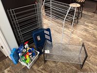Two metal shoe racks, gray laundry basket filled with cleaning products, and foldable clothes drying rack on floor
