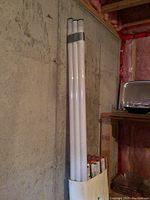 Photo of loose 2T12 fluorescent lightbulbs taped together in a cardboard box against a concrete wall.