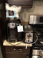 Photo showing Tassimo coffee machine alongside a pack of 100 paper coffee filters on top, and 2-slot toaster to the right on kitchen counter.