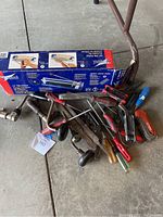 Overview of the boxed Capitol 13-inch tile cutter alongside various scrap and hand tools including screwdrivers, hammer, hand drill, and Allen keys.
