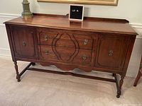 Front view of buffet showing carved drawer fronts, cupboard doors, brass hardware, scalloped apron and turned legs
