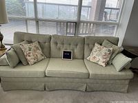 Front of pale green button back couch with four decorative pillows, set against windowed background.