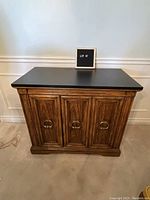 Front view of small wooden console with black top and three doors