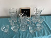 Full set of crystal ware arranged on blue cloth, includes pitchers, various stemmed glasses, and shot glasses