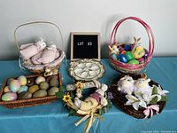 Full view of all Easter items in the lot on blue tablecloth, showing various baskets with eggs and plush animals, ceramic egg plate, and wreath with bunny and flowers.