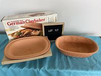 Photo of the clay baker base and lid placed next to the original box and lot sign