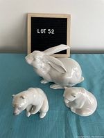 Photo showing one rabbit and two bear figurines from front view with 'LOT 52' sign in background