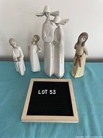 Photo showing four Lladro porcelain figurines standing upright on a blue surface, two nuns in the center and three girls on the sides.