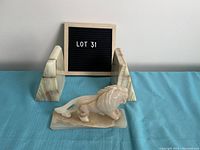 Front view of book ends and lion sculpture on blue cloth with lot sign behind