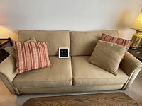 Front view of the creamy yellow upholstered couch with 4 pillows and two seat cushions.