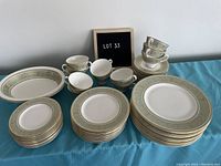 Full set of dinnerware items arranged on table: plates in three stacks, cups and saucers grouped, two oval platters