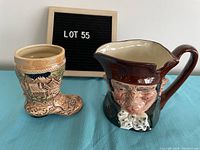 Front view of the Royal Doulton Old Charley stein with winking pirate face and the Bavarian boot ceramic mug side by side on a table.