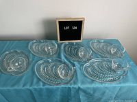 Top view showing all four sets of oval plates each with one matching clear glass cup, arranged in two rows on a blue cloth.
