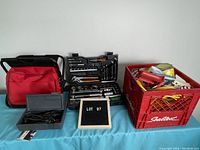 Overall view of the lot showing two tool cases and a red plastic crate with various tools and accessories on a blue cloth background.