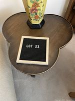 Top view of clover-shaped wooden side table showing surface wear and scratches with a floral patterned lamp base placed on top.