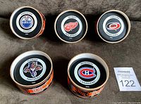 Top view of five NHL official game used hockey pucks in original packaging showing team logos for Edmonton Oilers, Detroit Red Wings, Carolina Hurricanes, Florida Panthers, and Montreal Canadiens.