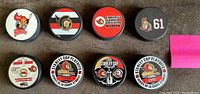 Top-down photo of all 8 Ottawa Senators souvenir hockey pucks arranged in two rows showing various team logos and commemorative designs.