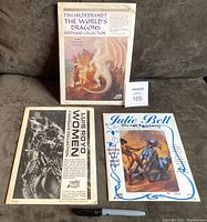 Photo showing all three sealed keepsake collections on a couch: Tim Hildebrandt "The World's Dragons," Luis Royo "Women," and Julie Bell "Metal Fantasy." Envelopes show some wear but remain sealed.