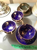 Three cobalt blue/gold cups and saucers and one forest green/gold cup and saucer displayed under lamp.