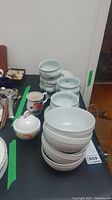 Porcelain bowls stacked with visible scratches, Queen's coffee mug, and Larry Laslo sugar bowl in front