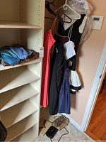 Multiple ladies dresses hanging on rack with several evening bags on floor and a light blue/purple scarf on shelf.