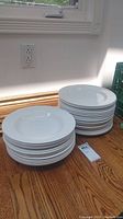 Two stacks of white ceramic dishes on wood surface, one stack of shallow bowls and one of plates.