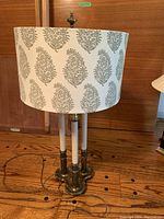 Front view of the lamp showing metal base with three candle-style light holders and fabric shade with leaf pattern.