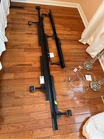 Black adjustable metal bed frame parts laid out on a hardwood floor showing caster wheels and support slats.