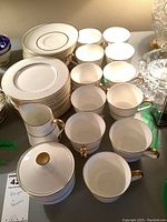 Top view of Mikasa Hunter pattern china items showing multiple dessert plates, 11 cups, cream and sugar set with gold trim on handles and rims.