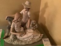 Front and side view of the Nao porcelain pastoral couple figurine showing the young man and woman seated together on a grassy base with floral details.