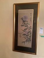 Framed print featuring purple flowers, bamboo stalks, and a bird, with Asian calligraphy on beige background inside gold frame and dark mat.