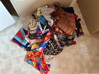 Pile of various ladies scarves in mixed colors, patterns, and fabrics on floor.