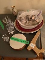 Top-down view of lot showing crystal elephant, silver napkin rings, cloisonné vase, china plates and bowl, crystal decanter stopper, and Swarovski mini vase labeled